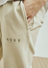 Load image into Gallery viewer, NORR Daisy sweat pants have a relaxed fit and tapered leg, with elastic in waist and hem. There is a subtle logo print on the front leg. Cotton